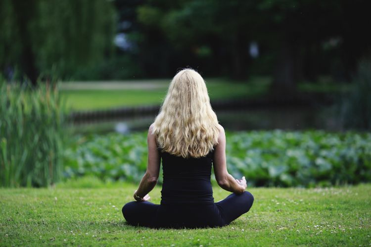 Pessoa branca sentada de costas na grama praticando o mindfulness